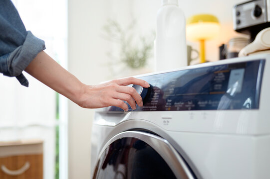 Woman pushing washing machine buttons for setting program or start laundry