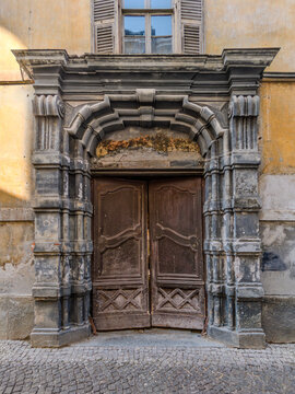 Detailed close-up of the weathered Baroque stone portal and historic wooden doors of Palazzo Chiodo, located in the old town of Cuneo, Piedmont, Italy.