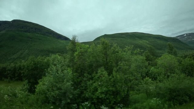 Driving side window view of traditional red barn with caravan and green mountains in Northern Norway