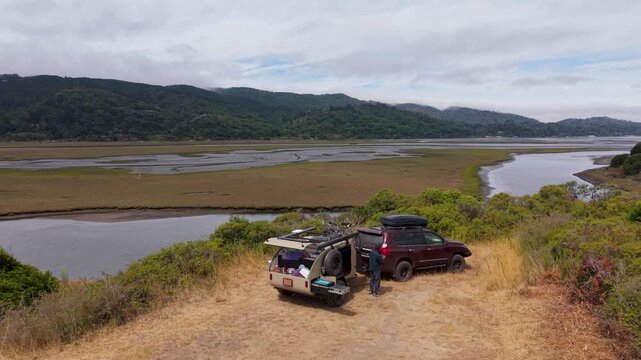 Views of teardrop camper trailer parked on roadside in California by a river during sunset. Adventure and freedom in nature.