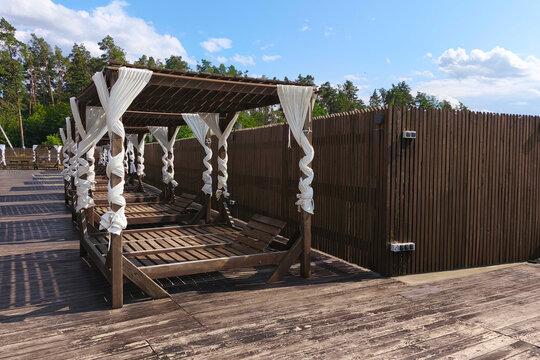 Luxury wooden cabanas with flowing white curtains on a sunny outdoor terrace. Elegant relaxation area at a modern resort, spa or poolside, featuring summer travel, leisure and vacation concept.