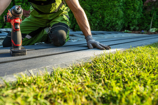 Worker installs decking boards on a sunny day in a backyard garden