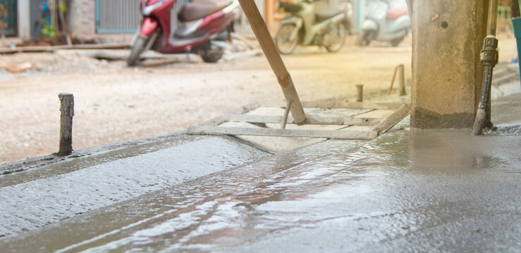 Construction workers use leveling tools for V-ditches or spoon drains, and to level wet concrete surfaces in road. Professional craftsmanship for urban infrastructure and pavement surface preparation.