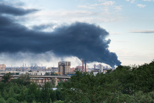 Large plumes of multiple tall black smokestacks rising in sky from asphalt factory in urban city, fire accident at chemical plant production facilities, industrial catastrophe and air pollution.