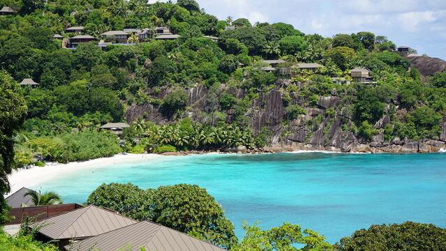 Idyllic private beach in a secluded green cove with granite boulders and hillside houses in Seychelles