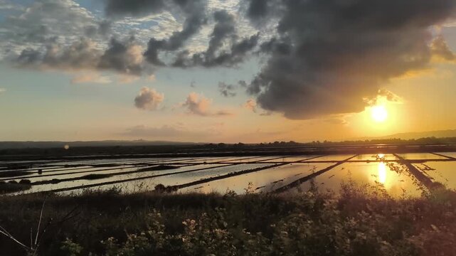 Traditional salt evaporation ponds reflecting vibrant sunset sky in rural coastal landscape at golden hour