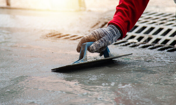 Mason hand in glove smoothing new concrete with a professional trowel tool. Skilled masonry worker performing surface finishing for pavement or sidewalk construction on site.