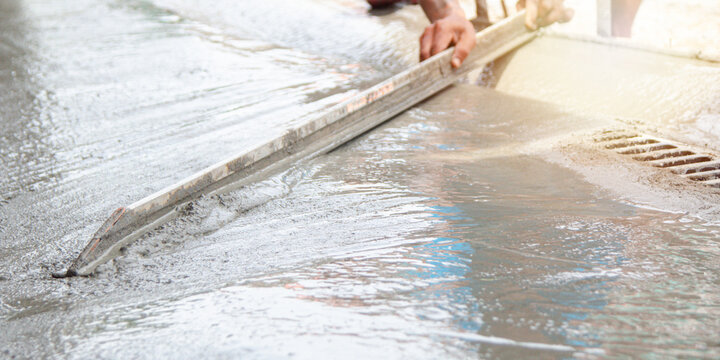 Close up of construction worker hands using an aluminum screed to level a new concrete floor. Professional masonry work and surface finishing for a building project or sidewalk repair.