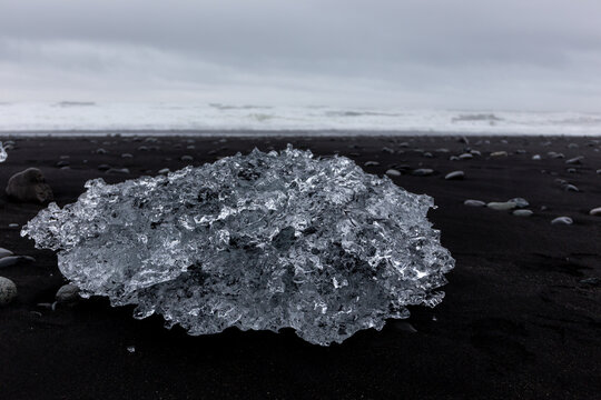 Transparent glacial iceberg block on black sand at Jokulsarlon Diamond Beach, Iceland