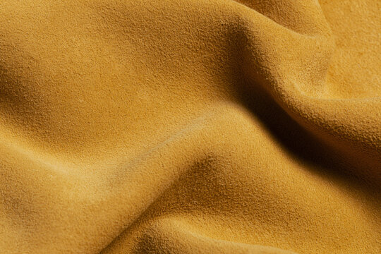 Background of draped warm yellow suede leather material with soft folds and textured surface