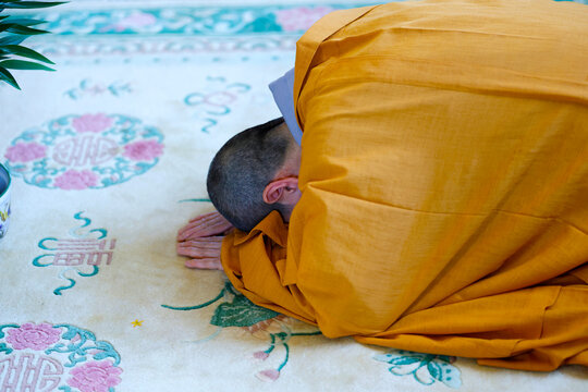 Tu An Pagoda. A Buddhist monk in an orange robe performs a prostration during a ceremony at a pagoda, expressing his faith and deep respect.