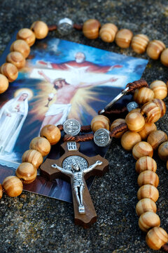 A rosary made of olive wood and a Corpus Christi cross placed on a religious image depicting the Holy Trinity and the Eucharist.