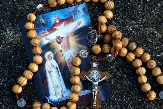 A rosary made of olive wood and a Corpus Christi cross placed on a religious image depicting the Holy Trinity and the Eucharist.
