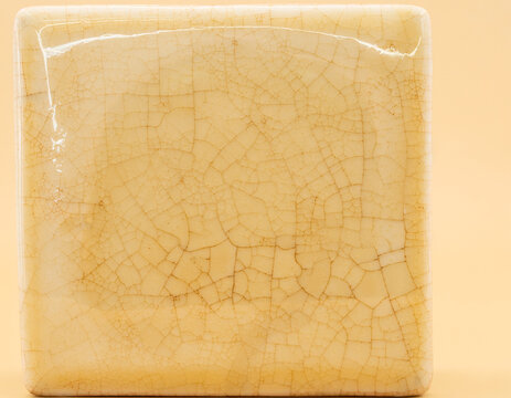 Glazed ceramic tile macro with deep crackle surface on solid warm ivory background