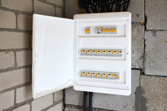 Electrical distribution board open on concrete brick wall with circuit breakers switches conduit wires for domestic power supply construction renovation house wiring system installation.