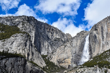 Bridalveil Fall cascades down towering granite cliffs in Yosemite National Park, California. Fresh snowfall blankets the surrounding Sierra Nevada peaks beneath dramatic blue skies and towering clouds © Gerard