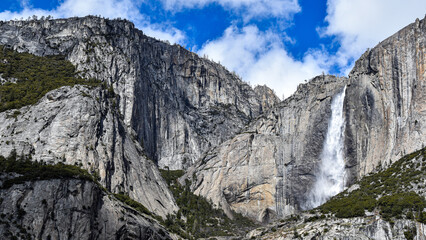 Bridalveil Fall cascades down towering granite cliffs in Yosemite National Park, California. Fresh snowfall blankets the surrounding Sierra Nevada peaks beneath dramatic blue skies and towering clouds © Gerard