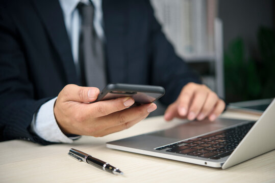 businessman holding smartphone working laptop computer office desk corporate communication digital business technology professional manager multitasking typing messaging network connection internet