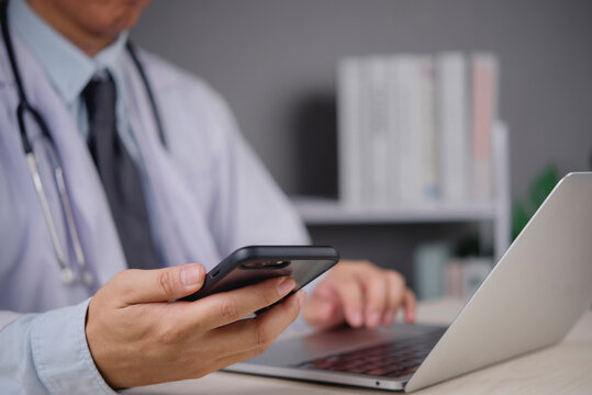 healthcare professional doctor working clinic office desk holding smartphone using laptop telemedicine online patient consultation medical application digital health communication technology device