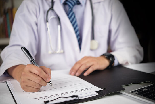 healthcare professional doctor signing document medical claim form health insurance hospital administration clinic desk filling paperwork patient treatment compensation legal finance record writing
