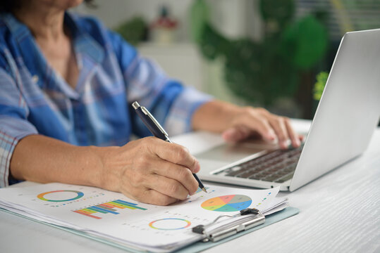 hands writing financial charts pen reviewing business statistics laptop desk analyzing market graph accounting budget investment planning working office report profit revenue statistics document