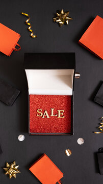 Black friday sale concept. Sale text in black gift box and shopping bags with festive decorations on black background flat lay, top view.
