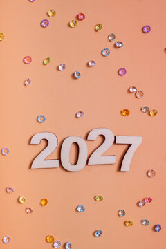 Wooden numbers representing the year 2027 placed on an orange surface with colorful confetti scattered around