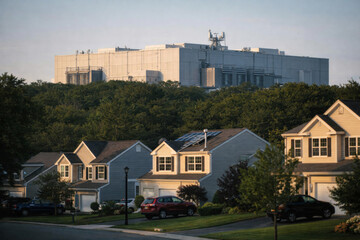 Suburban neighborhood in foreground with large data center visible in background © dvoevnore