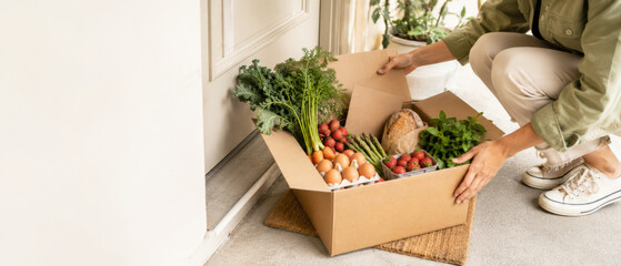 Fresh produce box with vegetables, eggs, and bread on doorstep, food delivery concept © dvoevnore