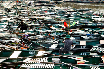 A large number of traditional boats are moored along a river. Men are preparing the boats for the day's work. Tam Coc, Vietnam. © Godong Photo