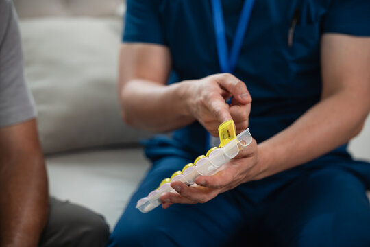 Caregiver Support for Senior Medication Management as a Male Healthcare Worker in Blue Medical Scrubs Reviews Medicine and an Organizer with an Asian Elderly Man at Home