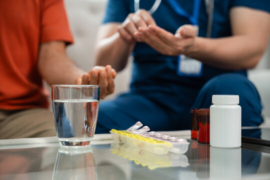 Caregiver Support for Senior Medication Management as a Male Healthcare Worker in Blue Medical Scrubs Reviews Medicine with an Asian Elderly Man at Home