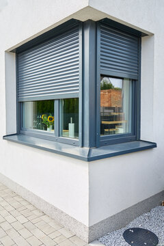 Partially lowered roller shutters cover two corner windows on a modern house, with kitchen items visible inside