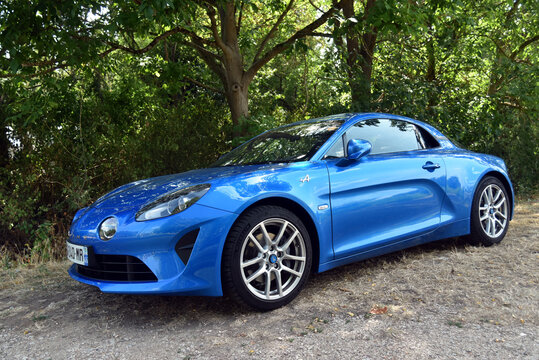 St- Amand Montrond - France - 2 August 2026 - Three quarter front side view of a blue Alpine A110 sports car parked at the edge of a forest