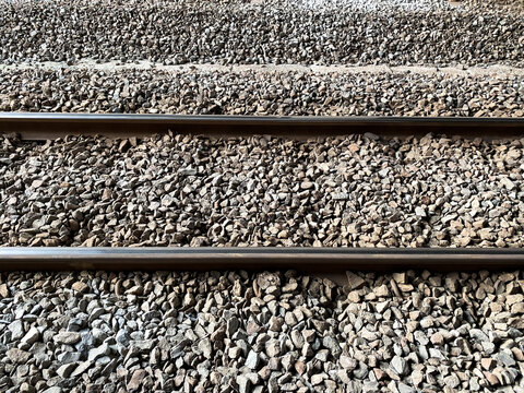 Top down view of parallel steel railway tracks running horizontally across a gravel ballast bed