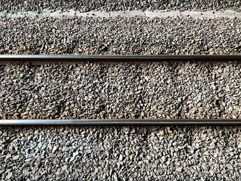 Top down view of parallel steel railway tracks running horizontally across a gravel ballast bed