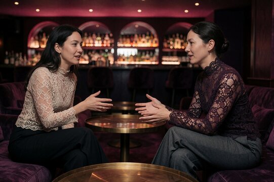 Two women conversing in an atmospheric underground lounge bar with burgundy lighting and bokeh background