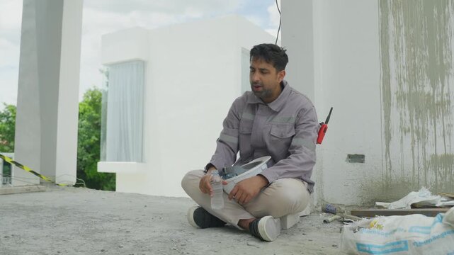 Home inspector construction site checking wall and floor surface, sitting concrete with tool and notebook, drinking water during building inspection near unfinished wall, seated floor with sample