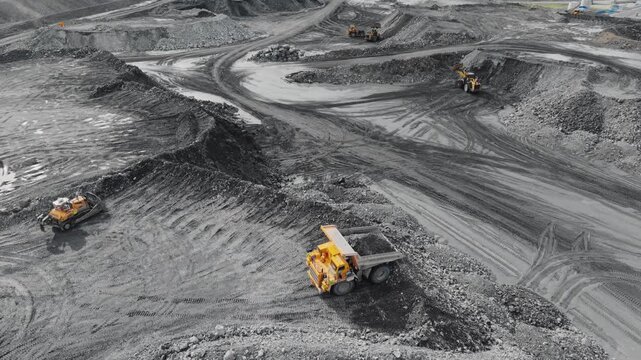 Aerial view of dump truck unloading gravel at open pit quarry on muddy haul roads with excavators and loaders. tracking pan tilt.
