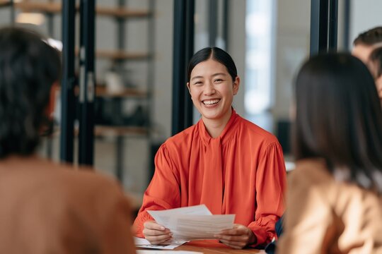 Smiling woman in red blouse leading a small group meeting and holding papers for corporate presentation background and team collaboration in office