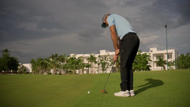 Focused male golfer making a putt on a beautiful golf course with a dramatic cloudy sky