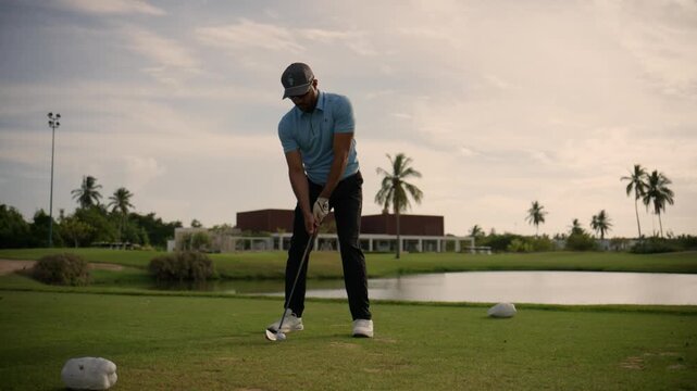 Athletic man playing golf on a beautiful green course with palm trees and a lake in the background
