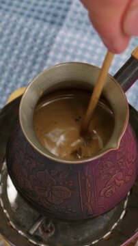 A hand uses a wooden stick to stir brewing Turkish coffee inside a decorated copper cezve pot. Concept of artisanal beverage preparation, morning energy, coffee culture, and authentic craftsmanship