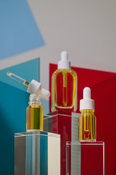 Three glass dropper bottles with yellow liquid on clear pedestals
