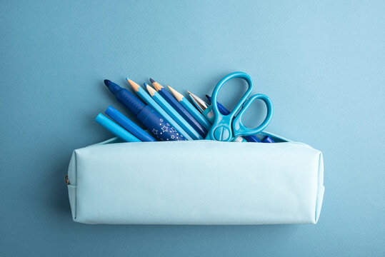 Blue pencil case overflowing with assorted writing and drawing supplies including pencils pens and scissors