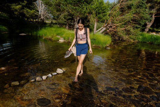 Athletic young woman crossing a small river barefoot