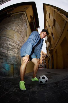 Young man prepares to kick soccer ball in narrow street