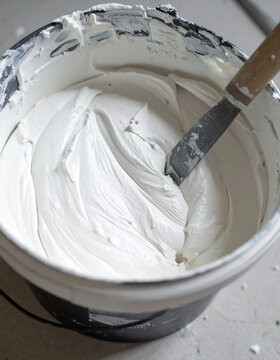 Freshly mixed smooth white plaster inside sturdy construction bucket with metal trowel, ready for wall application, construction and renovation concept. Close-up.