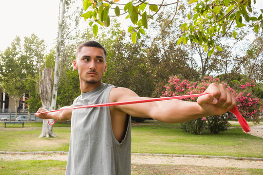 Young Man Stretches Resistance Band in Park During Afternoon