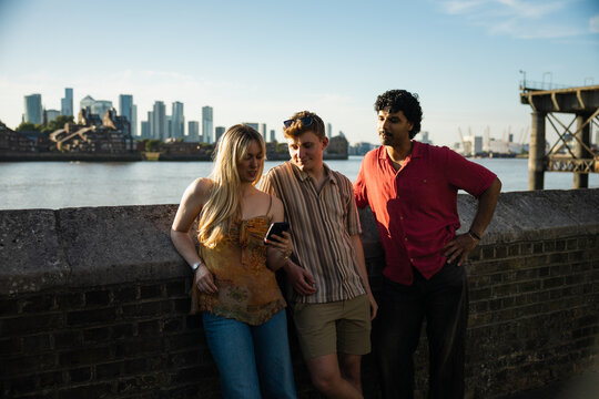 Friends looking at a smartphone screen by the River Thames